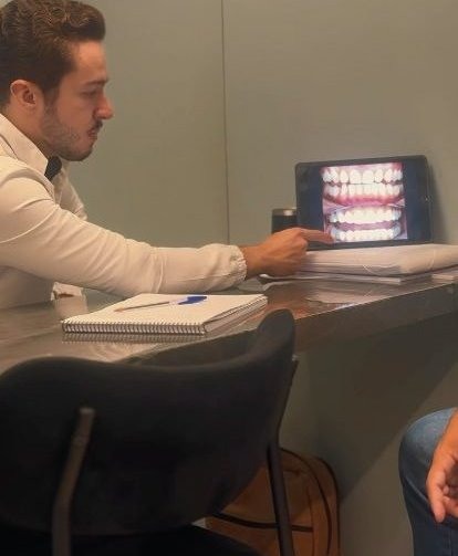 Dr. Rafael Melo explicando o plano de tratamento ao paciente, com simulação do sorriso na tela
